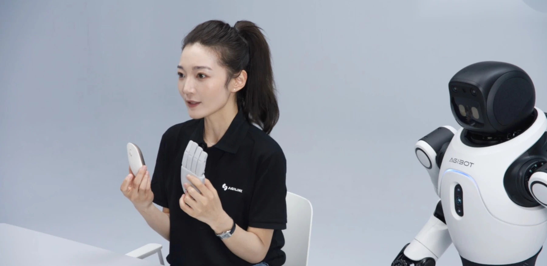 AGILINK presenter holding the complete small Lite-S hand beside a compact humanoid